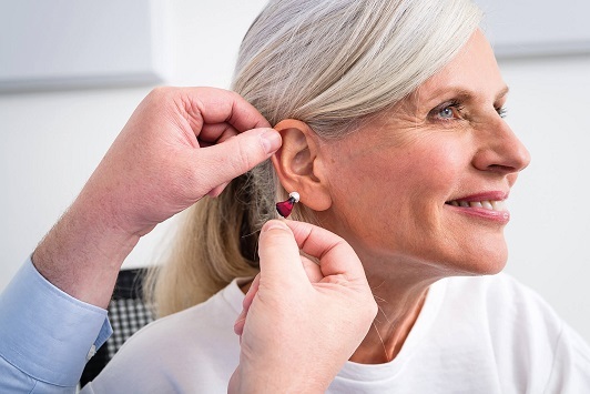 Eine Frau bekommt ein Hörgerät eingesetzt, Hörakustiker passt Hörhilfe an ihr Ohr an.